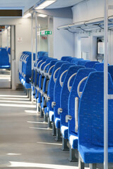 Fototapeta premium Interior of modern passenger high-speed express train, row of empty blue fabric soft seats selective soft focus. Inside the train carriage with comfortable and colorful chairs. Public transportation