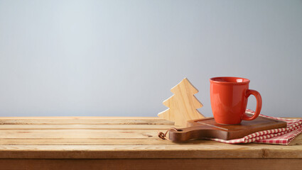 Wooden table with coffee cup, cutting board, tablecloth  and Christmas decoration over gray wall background.  Kitchen mock up for design and product display.