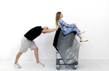 a gray-haired man barely pushes a stack of metal black chairs on which a young woman sits. High...
