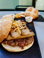 Close-up of a beef burger, fries and sausages on a terrace on a slate plate.