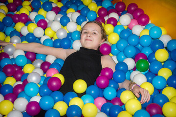 Little cute girl has fun playing with colorful plastic balls.