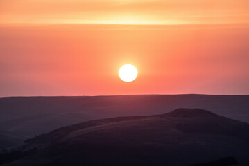 Beautiful late Summer sunset landscape image of setting sun kissing the horizon in the Peak District, viewed from Higger Tor