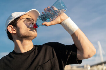 Drinking clean water from a bottle, a male athlete training in the city in sportswear.