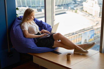 Businesswoman sits on the windowsill while working on a gadget
