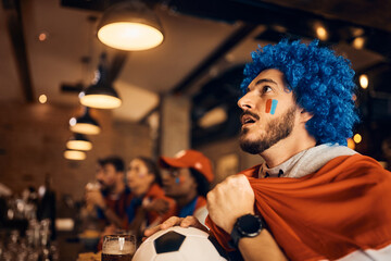 Young soccer fan anticipating his team's victory while watching game in pub.
