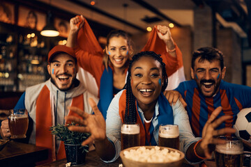 Excited fans cheering for their team while watching sports match in bar.