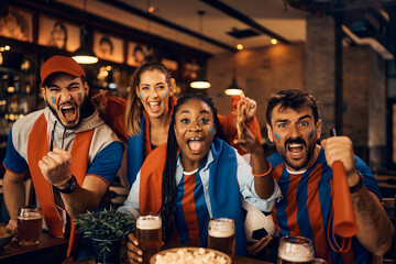 Passionate sports fans cheering while watching match in pub.