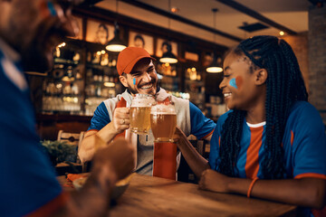 Happy sports fan toasting with his friends while drinking beer in bar.