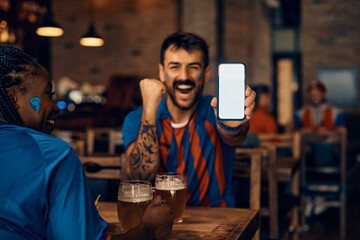 Close up of happy sports fan showing smart phone with blank screen while celebrating victory of his...