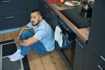 Thoughtful asian man sitting in the kitchen on the floor