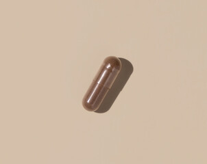 Brown Medical capsule on light beige top view, hard shadows. Taking dietary supplements