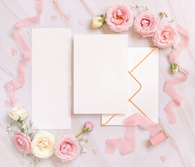 Obraz na płótnie Canvas Blank paper cards between pink roses and pink silk ribbons on pink top view, wedding mockup
