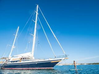 middle-aged woman practicing paddle surf next to a sailboat, Ses Covetes beach, Majorca, Balearic Islands, Spain