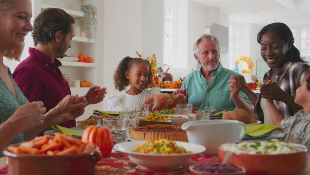 Multi-generation family joining hands to say prayer before enjoying Thanksgiving meal together - shot in slow motion