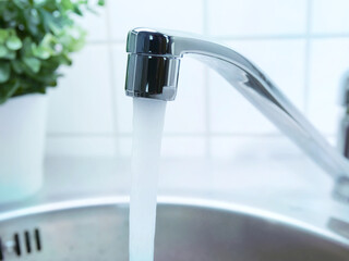 A stream of clean water drink flows from the kitchen faucet into the stainless steel sink. Environment, water pollution and water shortage concept