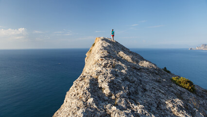 A lonely figure of a walking girl on a narrow triangular cliff on the Southern coast of Crimea