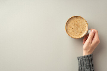 Fototapeta Autumn concept. First person top view photo of young woman's hand in sweater holding cup of frothy coffee on isolated grey background with empty space obraz