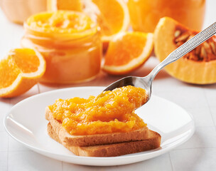 Roasted toasts bread with spoon of pumpkin jam. Pumpkin puree in jar, slices of orange and pumpkin on wooden background. Autumn thanksgiving. Ingredient for autumn dessert. Top view.