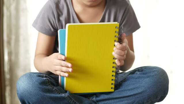 child girl holding many colorful notepad sited on chair 