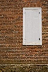 19th century white shuttered window in brick wall.