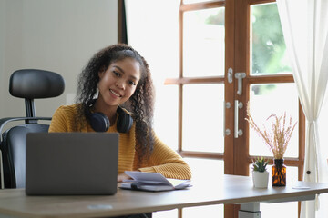 Smiling young African American woman in headphones distracted from computer work look in distance dreaming. Happy biracial female study online at home on laptop thinking or planning. Vision concept.