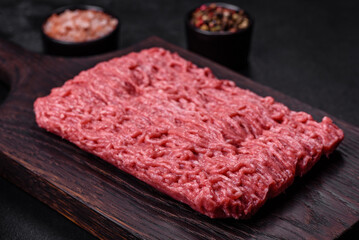 Fresh minced beef on cutting board on dark background with ingredients for cooking