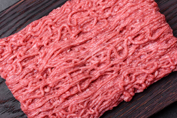 Fototapeta premium Fresh minced beef on cutting board on dark background with ingredients for cooking