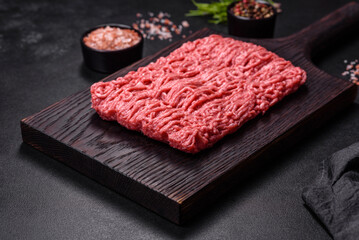 Fresh minced beef on cutting board on dark background with ingredients for cooking