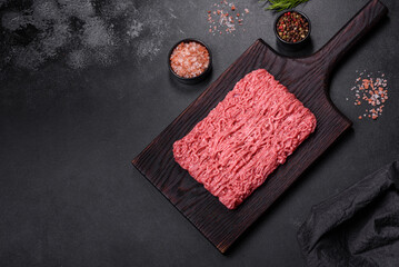 Fresh minced beef on cutting board on dark background with ingredients for cooking