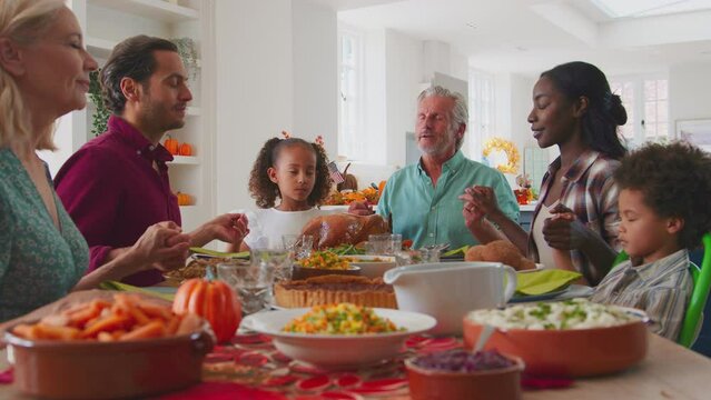 Multi-generation family joining hands to say prayer before enjoying Thanksgiving meal together - shot in slow motion
