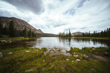 The beautiful expanse of Mirror Lake in the Uintas National Forest, surrounded by bright green trees and foliage under a cloudy, even diffuse sky