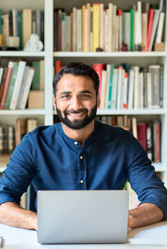 Happy Smiling Indian Ethnic Professional Business Man Teacher Sitting At Work Desk With Laptop Computer Remote Working At Home Office Or Learning Online, Vertical Portrait. Business Education Concept