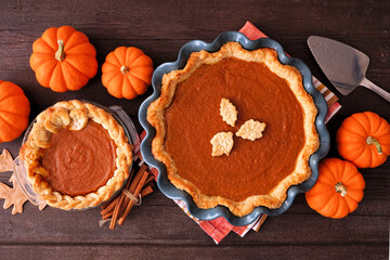 Homemade fall pumpkin pies. Above view table scene on a dark rustic wood background.