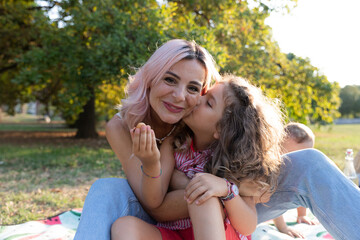 Daughter gives a kiss to her mother during a picnic, love between mother and daughter.