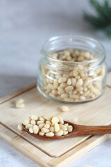 A wooden spoon with pine nuts lies on a wooden board. Behind is a jar of pine nuts, also a branch of cedar. selective focus
