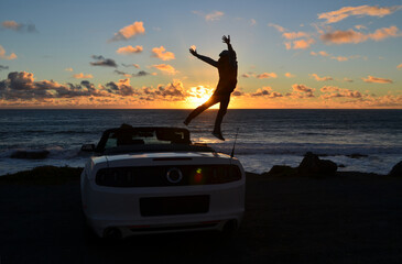 Silhouette of a person jumping off a car on the beach during sunset