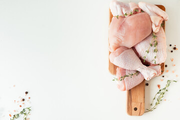 Raw uncooked chicken meat on a wooden cutting board with spices and herbs. Top view of chicken thigh, leg, fillet and wings on the white background. Free space