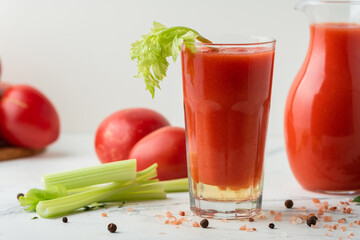Fresh tomato juice in a glass with a straw on the white background. Red tomato juice cocktail with tomatoes and celery