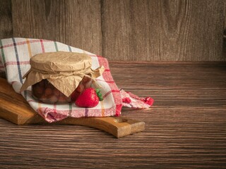 A closed jar of strawberry jam on a wooden board and napkins, fresh berries. Tied with jute rope and parchment. Conservation, winter supplies