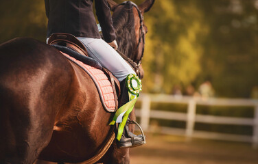 On a bay horse in the saddle sits a rider with a green rosette of the winner in equestrian...
