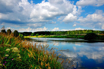 Lake clouds. Beautiful summer landscape, meadow flowers bloom on the hillsides, clouds in the sky, clouds reflected in the water, a serene warm summer day. Moscow region, Russia. 