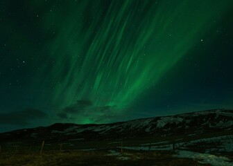 Fototapeta premium Scenic shot of the Aurora Borealis above snowy-covered mountains during nighttime