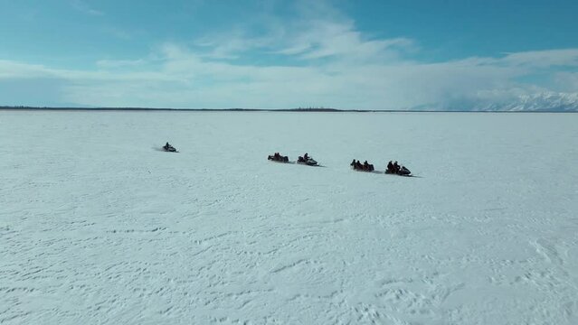 snowmobiles riding follow each other in minimalistic arctic landscape against the blue sky