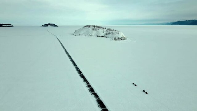 panoramic view of a couple snowmobile follow each other towards the island in endles winter landscape of a frozen bay of winter Baikal lake