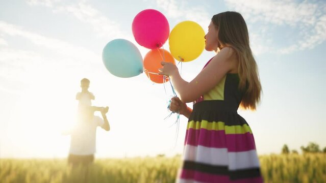 happy family on holiday in the park with balloons. father wears his son playing in a field with wheat in nature in the park. girl with balloons kid concept. dream friendly family at a birthday party