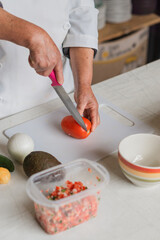 Detail shot of a woman's hands cutting a tomato on a board with onion and avocado.