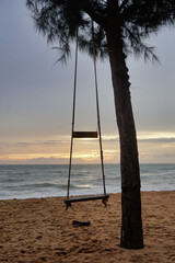Vertical picture of a swing chair tied to a tree with a backdrop of the evening sea and the setting sun.