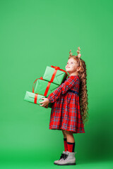 cute little girl of 7 years old with curly hair in golden deer horns, standing with gift boxes on a green background in the studio. the child smiles happily and looks away. Advertising. copy space