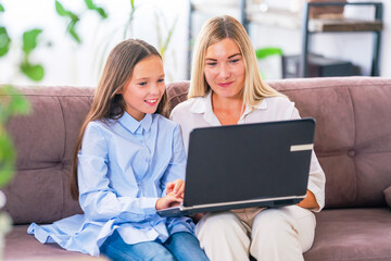 Happy mom and teenage daughter, sitting and relaxing on couch at home, using laptop together, browsing Internet on computer. engaged in shopping, communicate with relatives. trained in new application