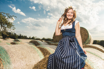Beautiful woman in a traditional bavarian dirndl dress posing on a hay bales background.  - obrazy, fototapety, plakaty